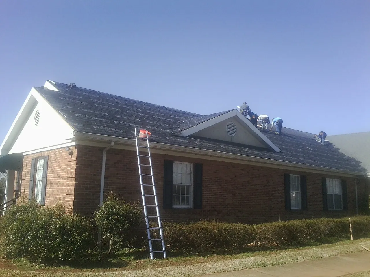 Crew tearing shingles off a brick ranch roof with a ladder set — Metal Roof Repair work by our crew in Picacho