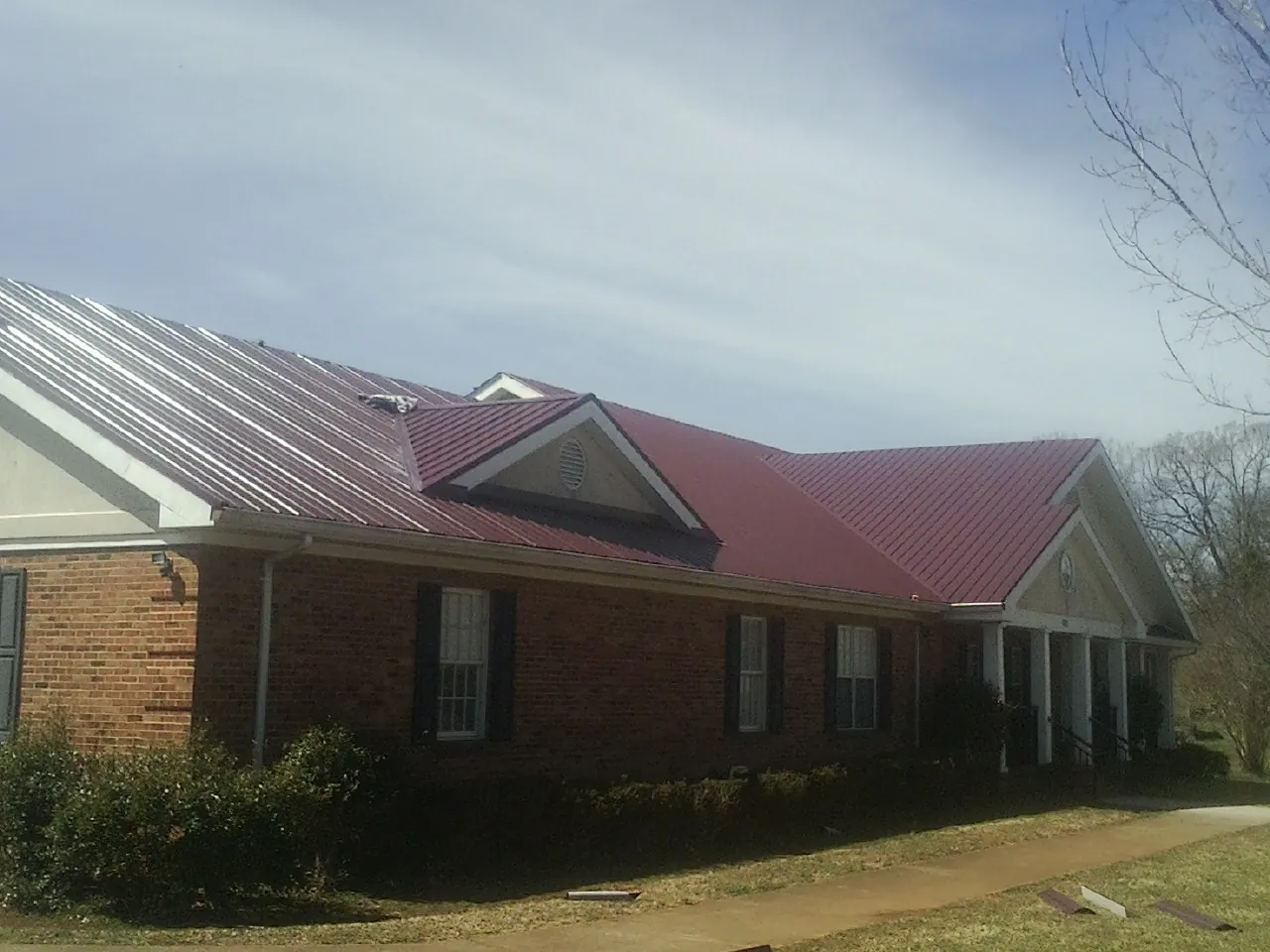 Red metal roof with gabled entries on a long brick building, from a Hail Damage Roof Repair job in Picacho