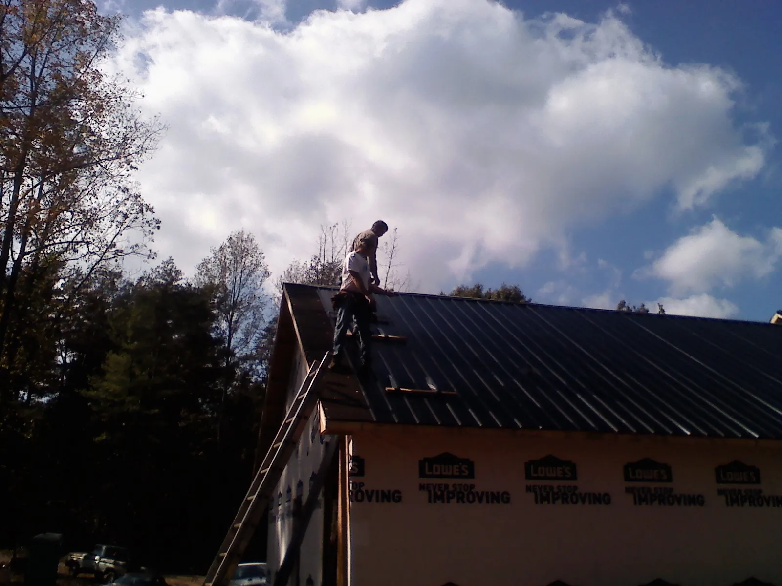 Roofer fastening dark metal panels high against a cloudy sky, from a Roof Inspection job in Picacho